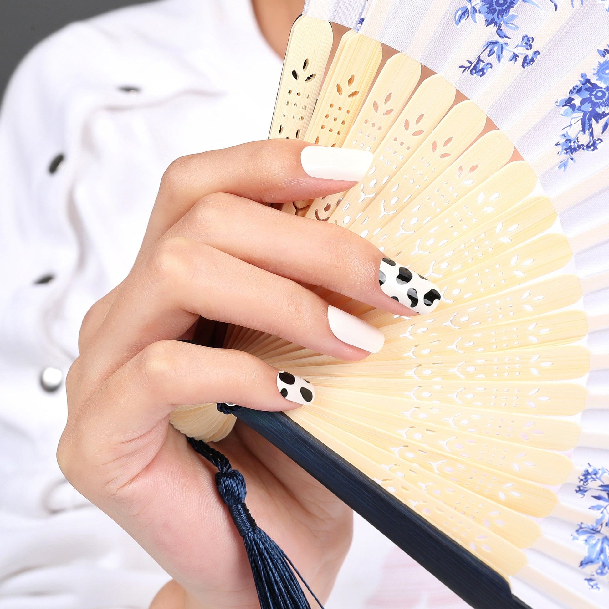 Hand holding decorative fan wearing black and white cow print nail wraps animal pattern manicure