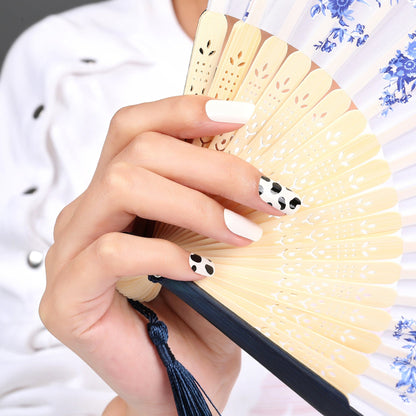 Hand holding decorative fan wearing black and white cow print nail wraps animal pattern manicure