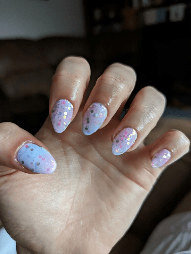 Pastel pink blue glitter nail wraps on hand displaying celestial gradient nail art design