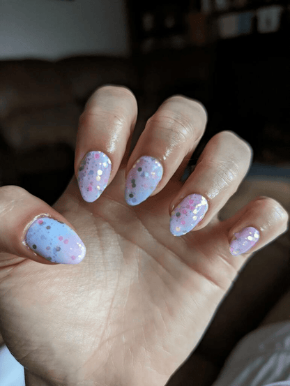 Pastel pink blue glitter nail wraps on hand displaying celestial gradient nail art design