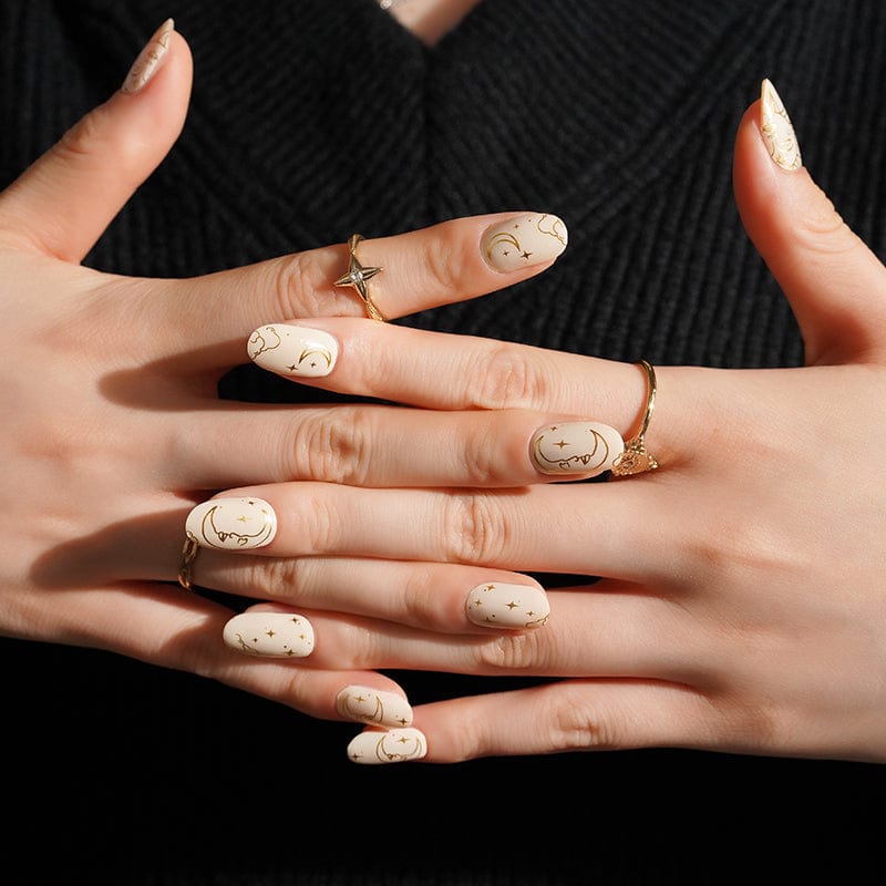 Celestial nail wraps on hands featuring gold moon and star line art on nude base