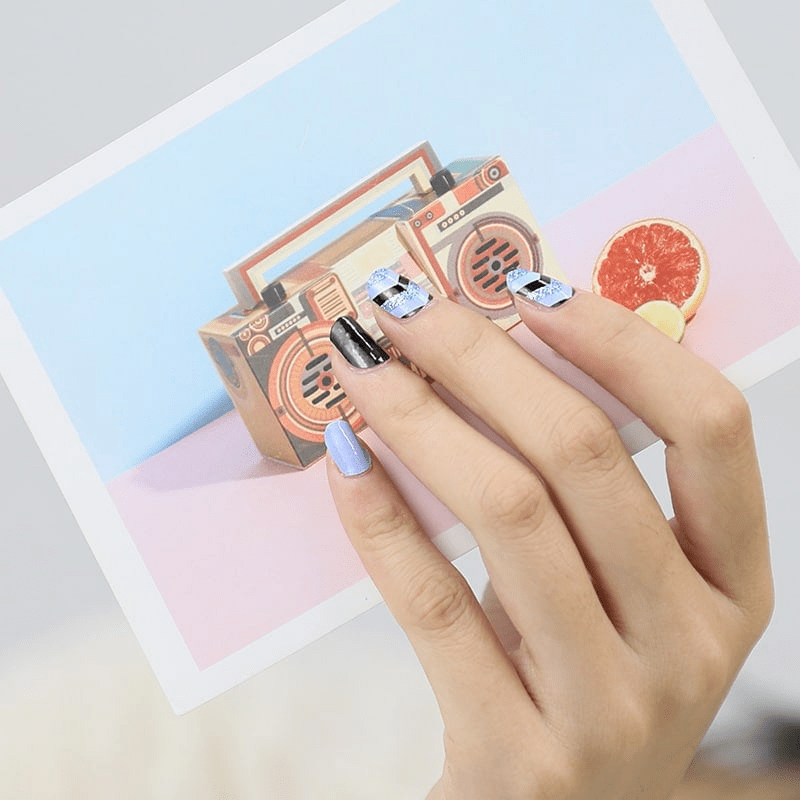 Hand with geometric nail wraps holding vintage radio beside colourful paper backdrop