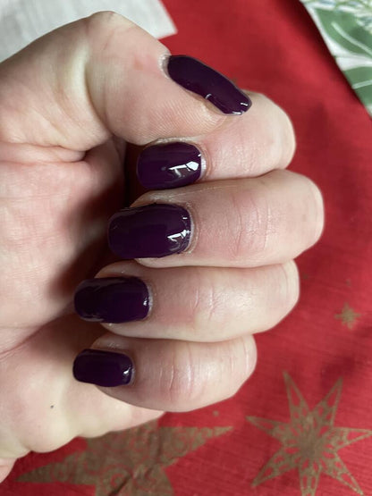 Hand wearing deep berry purple nail wraps with high gloss finish autumn manicure style