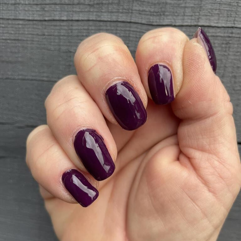 Hand showing rich mulberry purple gel nail wraps with glossy finish professional manicure look