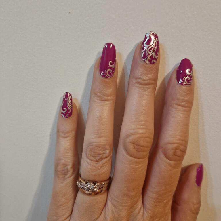 Hand wearing purple nail wraps with silver ornate baroque pattern decorative manicure