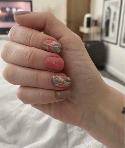 Hand displaying coral pink nail wraps with gold foil feather pattern mixed design manicure