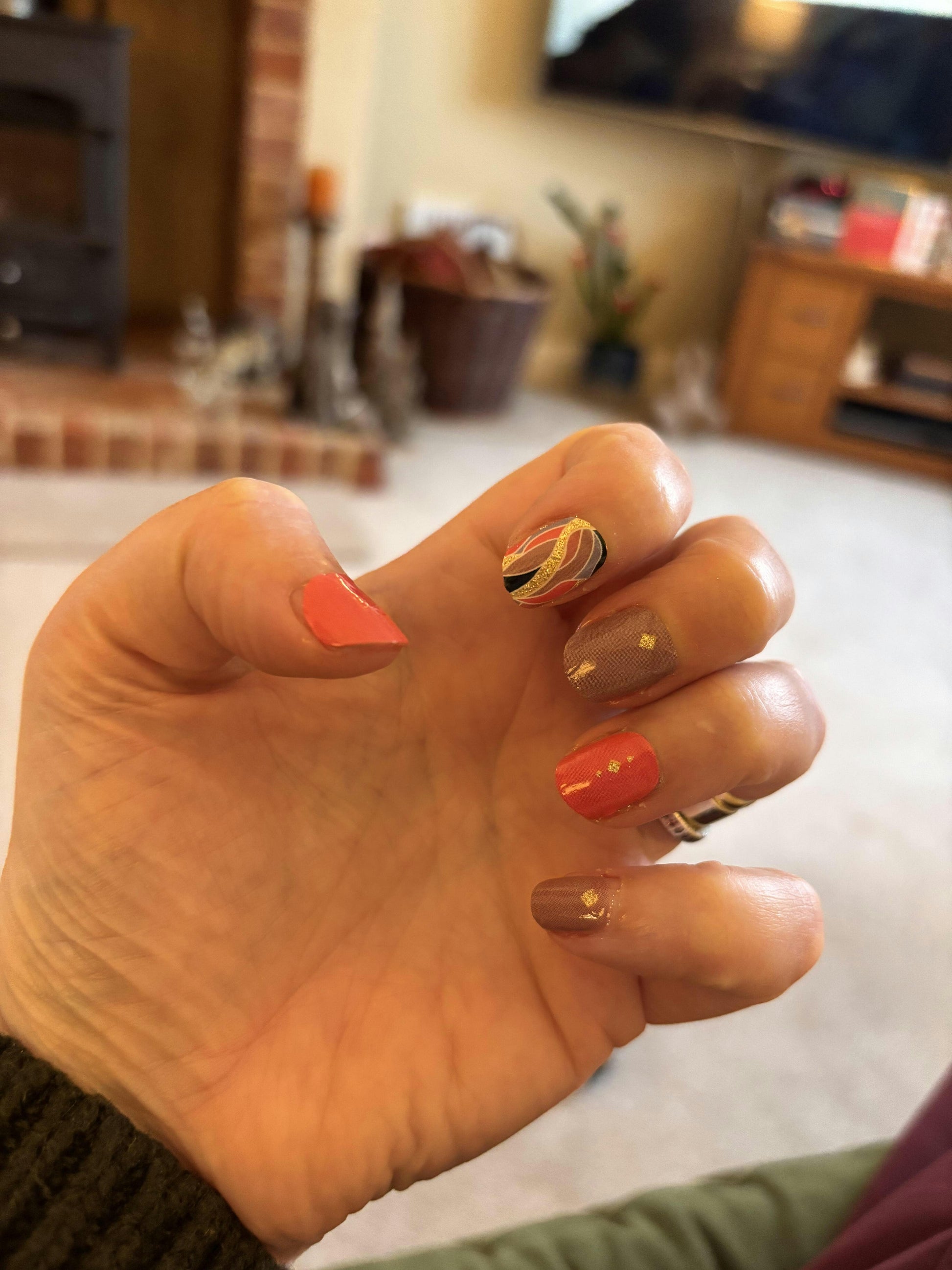 Hand displaying coral and brown nail wraps with gold foil feather pattern at-home manicure