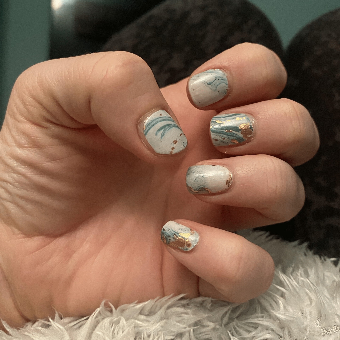 Hand wearing blue and gold marble nail wraps with abstract watercolour stone effect