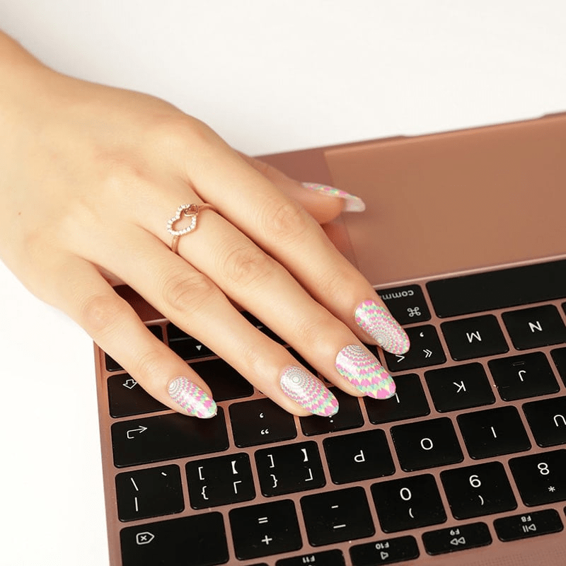 Hand typing on laptop wearing multicoloured geometric nail wraps with psychedelic optical illusion design