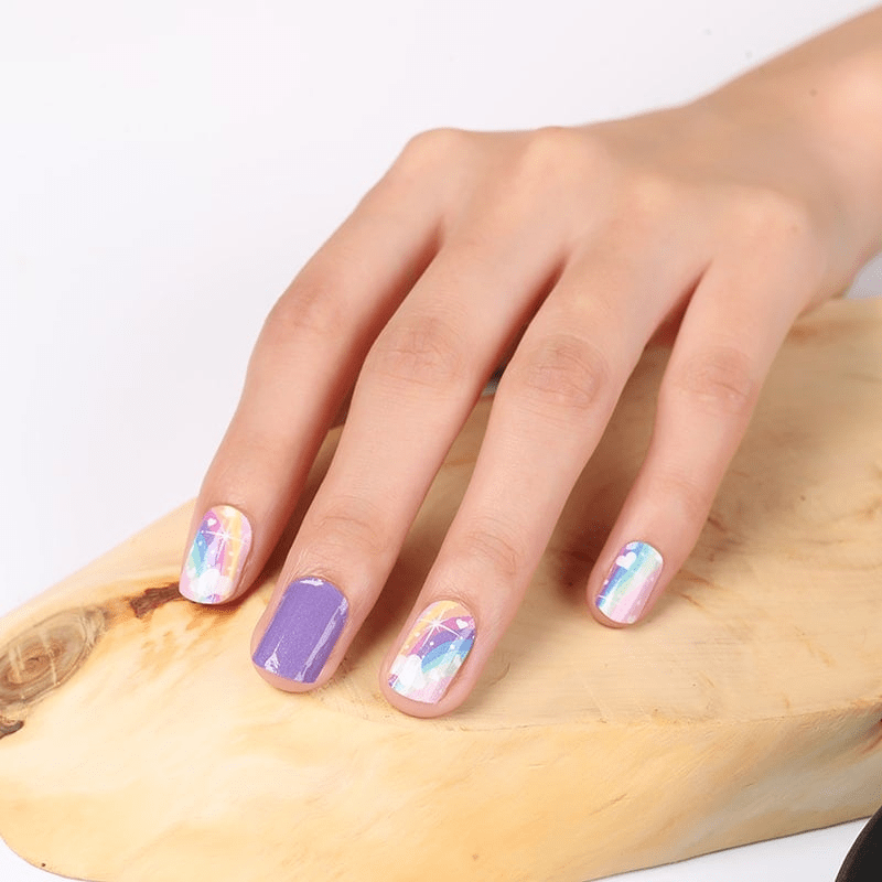 Hand wearing rainbow gradient non-UV nail wraps with pastel purple pink and holographic star patterns