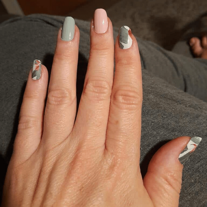 Hand displaying botanical nail wraps with sage green base and white palm leaf pattern designs