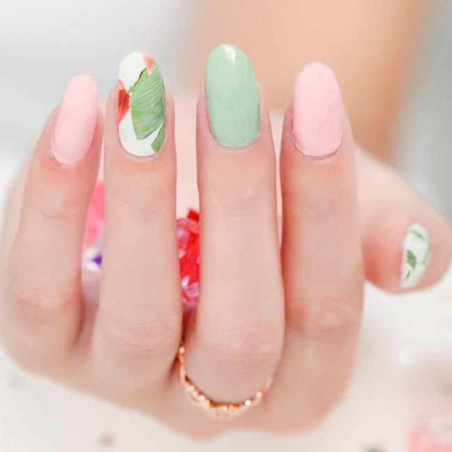 Hand wearing tropical nail wraps featuring sage green solid colour and palm leaf botanical patterns