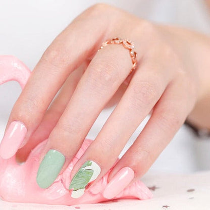 Close-up of gel nail wraps in sage green and peach with tropical palm leaf nail art