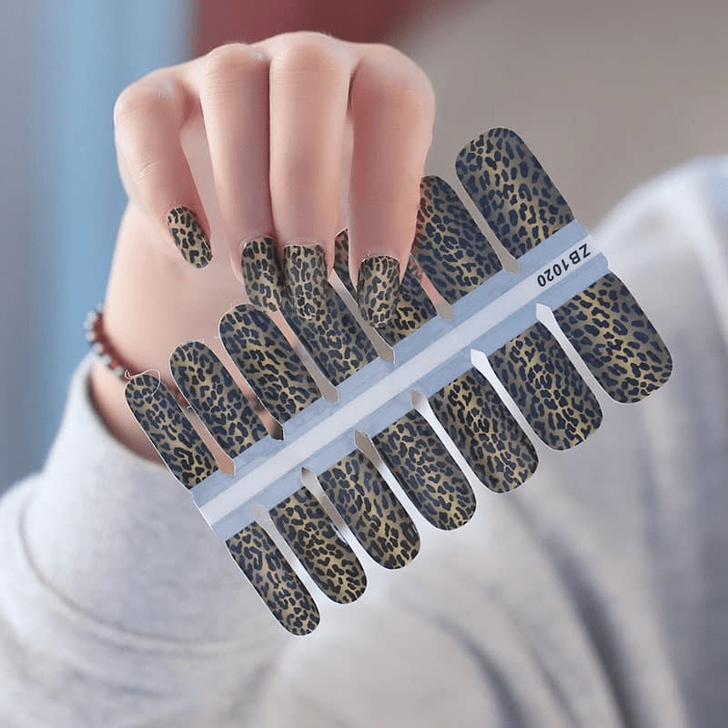 Hand displaying leopard print nail wrap sheet with brown and tan animal pattern