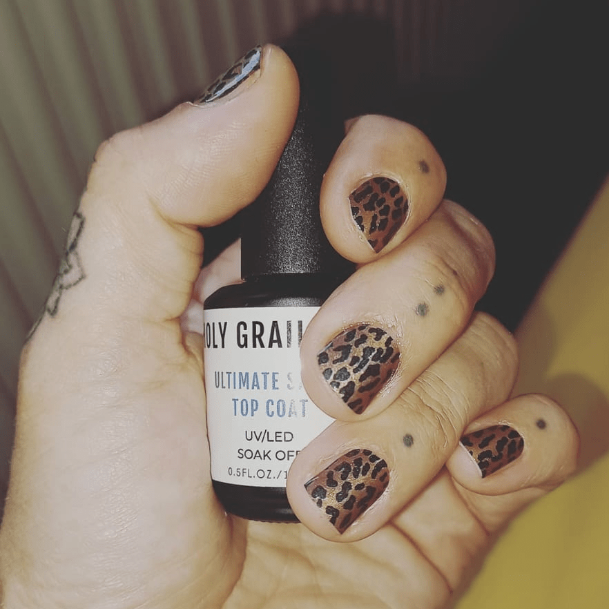 Hand holding nail glue bottle wearing leopard print nail wraps in brown and tan