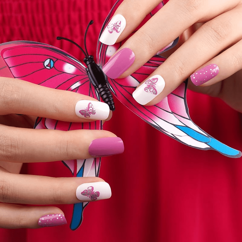 Pink butterfly nail wraps with polka dots displayed on hands with decorative butterfly prop