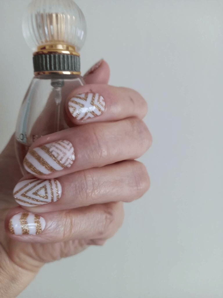 Hand wearing pink nail wraps with gold glittery geometric chevron patterns for elegant manicure