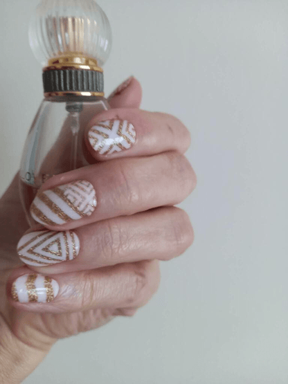 Hand wearing pink nail wraps with gold glittery geometric chevron patterns for elegant manicure