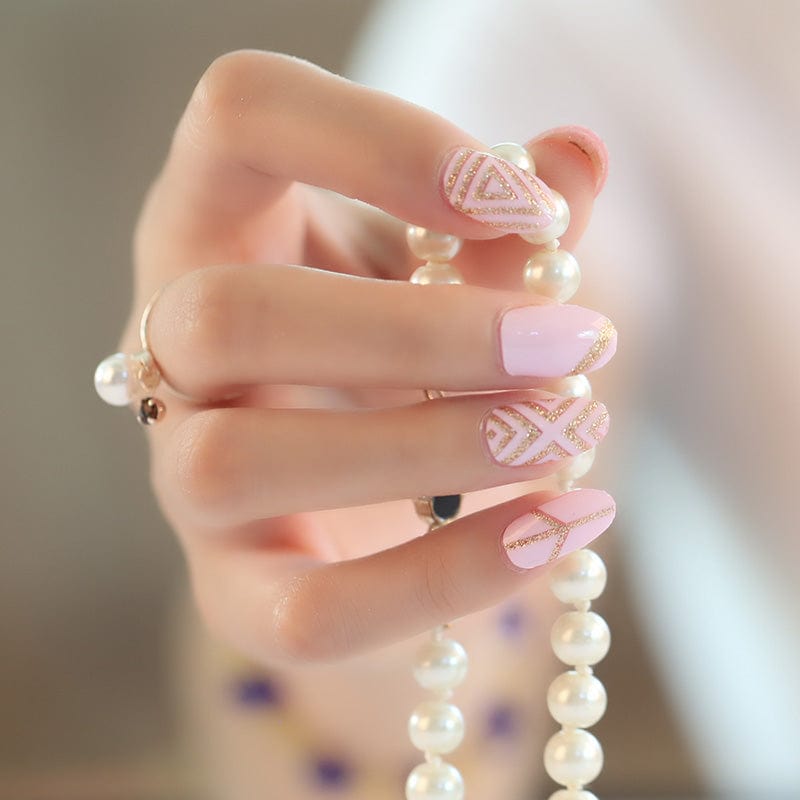 Pink nail wraps with gold geometric designs on hand holding pearl necklace
