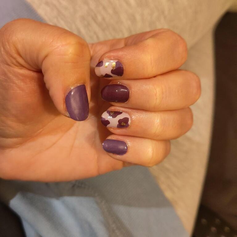 Hand wearing purple leopard print gel nail wraps with burgundy animal pattern design