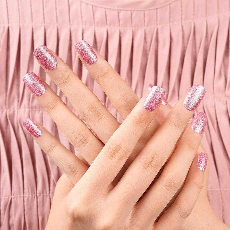 Two hands displaying pink glitter nail wraps for DIY manicure