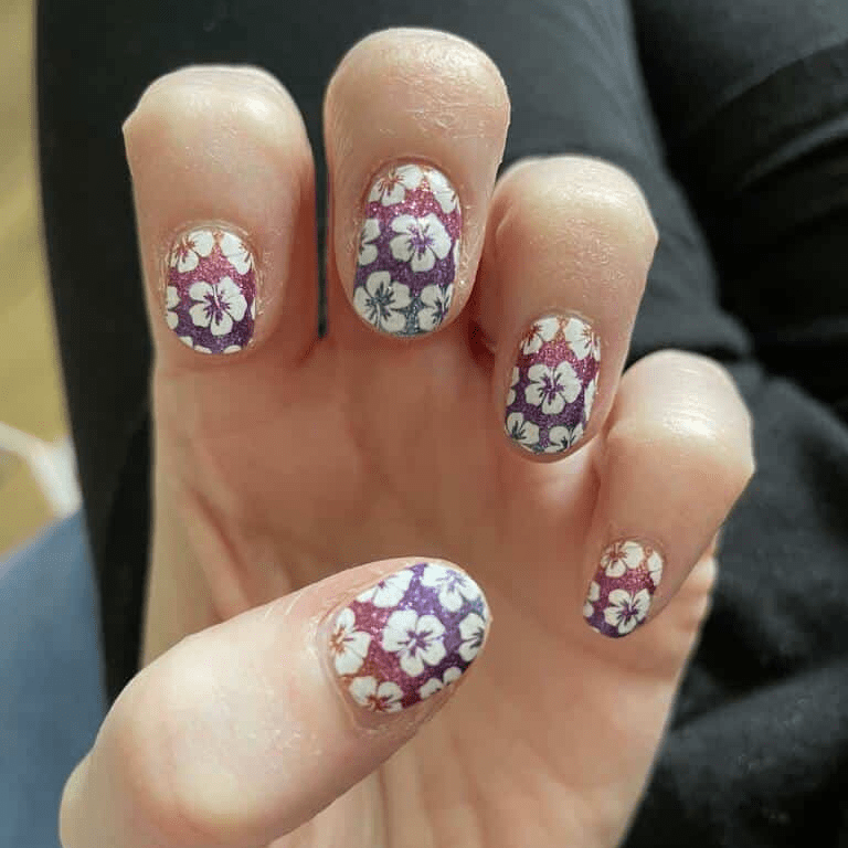 Floral patterned nail wraps on hand featuring purple hibiscus flowers with ombre gradient design