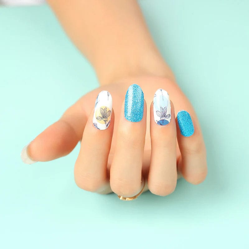 Blue glitter and white botanical leaf gel nail wraps displayed on hand against mint green background