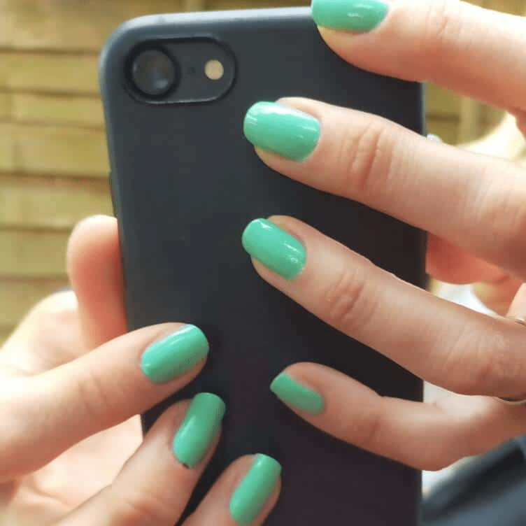 Mint green gel nail wraps on hand holding black phone for at-home manicure