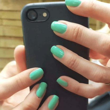 Mint green gel nail wraps on hand holding black phone for at-home manicure