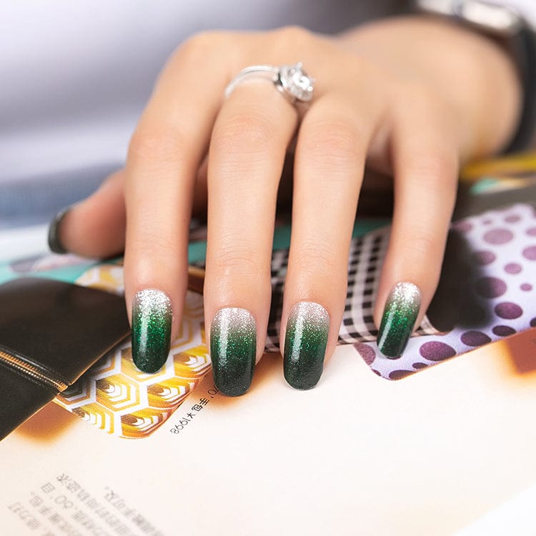 Emerald to silver gradient gel nail wraps on hand with diamond ring and magazine