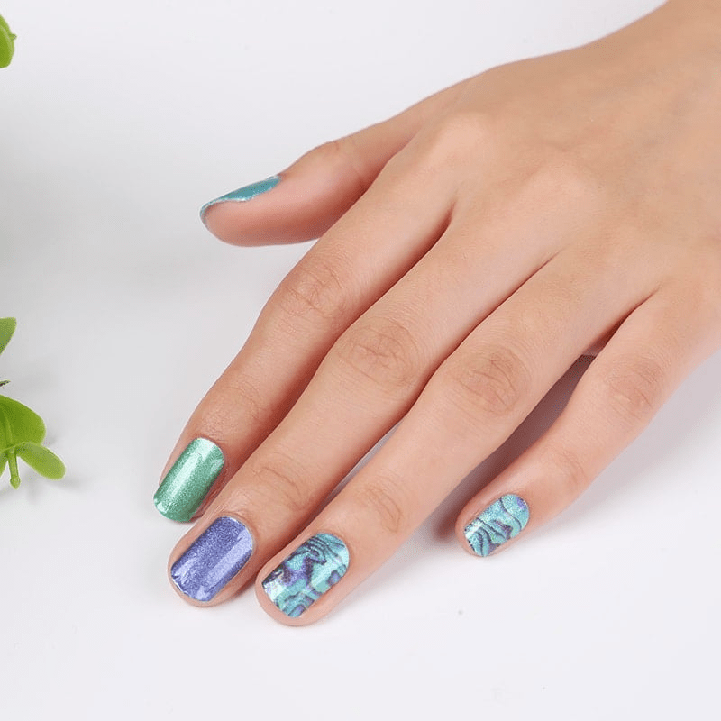 Hand displaying blue and teal marble nail wraps with metallic shimmer finish