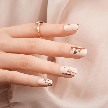 Beige nail wraps with gold metallic foil design on manicured hand