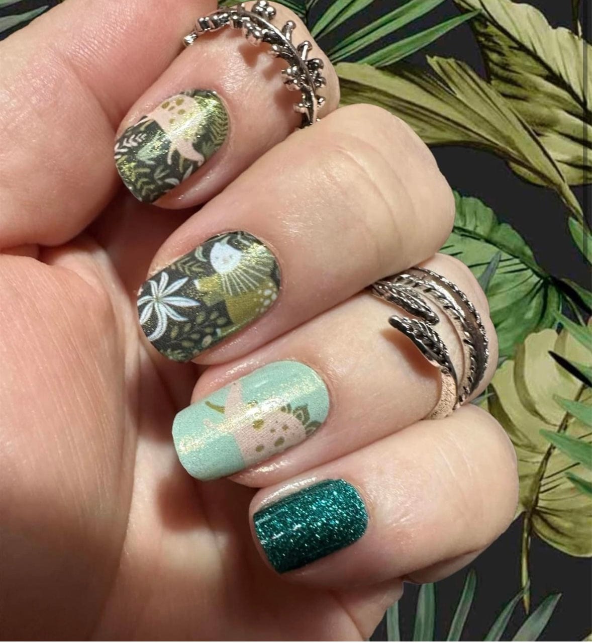 Dinosaur themed nail wraps on hand in sage green with glitter and prehistoric patterns