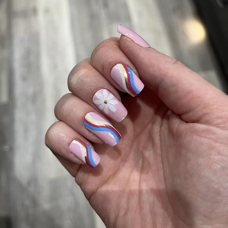 Pink nail wraps with white daisies and rainbow stripes applied on hand showing manicure