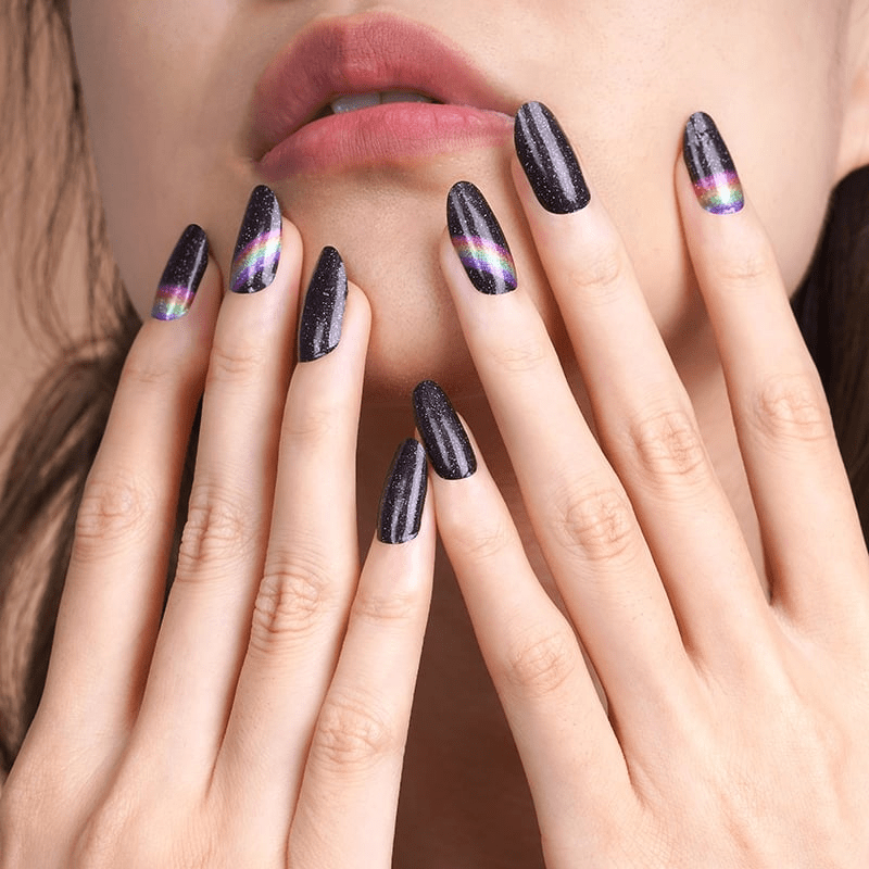 Black glittery nail wraps with rainbow holographic stripes on hands near lips
