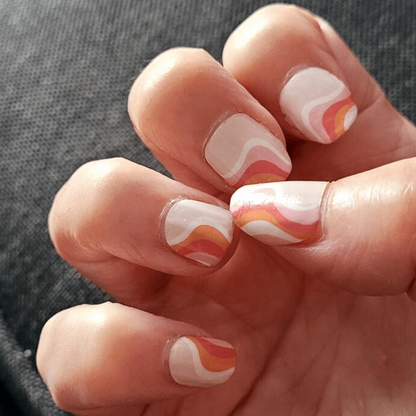 Hand wearing coral pink non-UV nail wraps with flowing cream swirl pattern nail art design