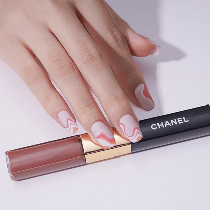 Manicured hand with pink marble nail wraps holding lipstick showing elegant swirl pattern design