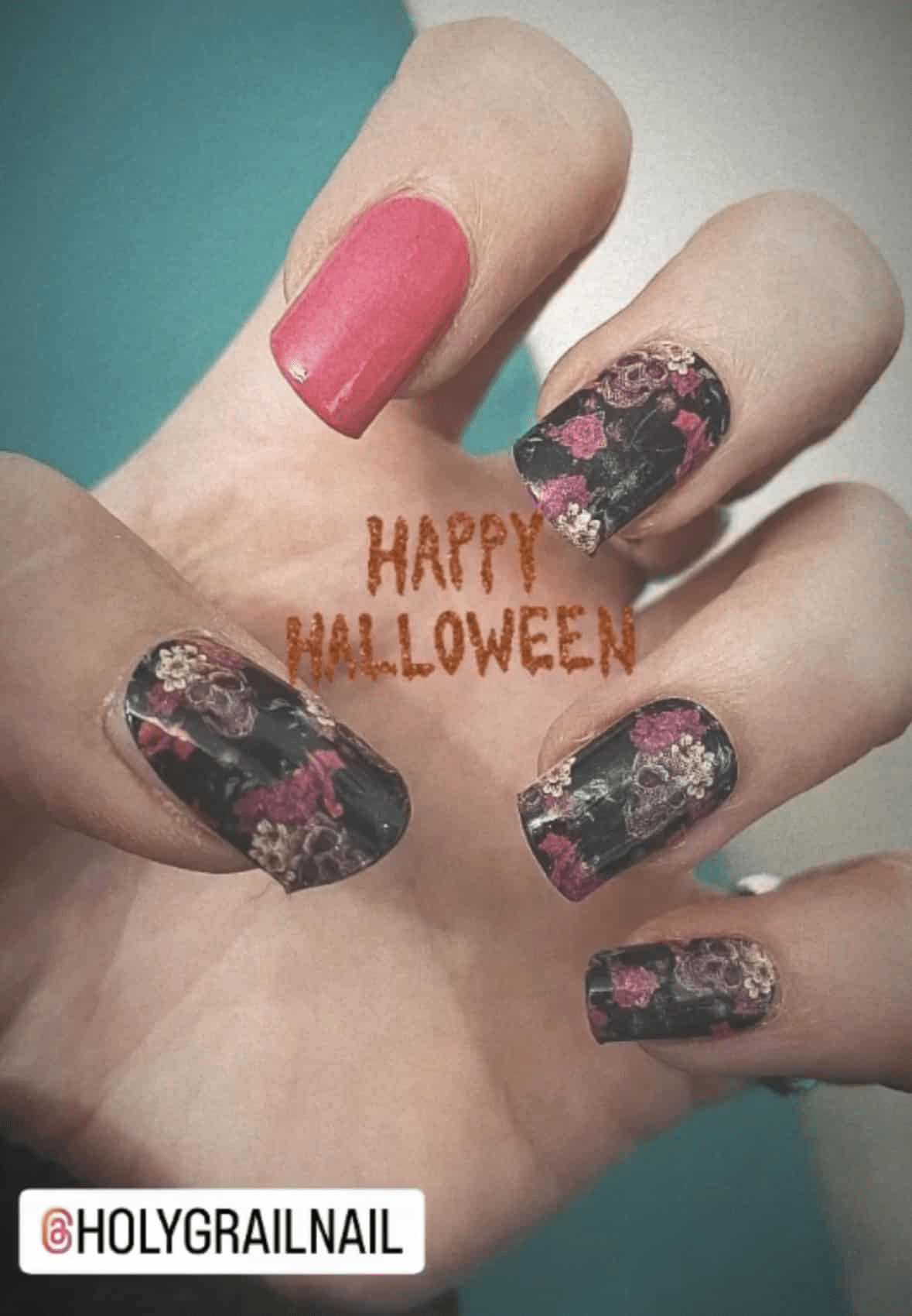 Black gothic nail wraps with pink roses and skull designs on hand showing Halloween nail art