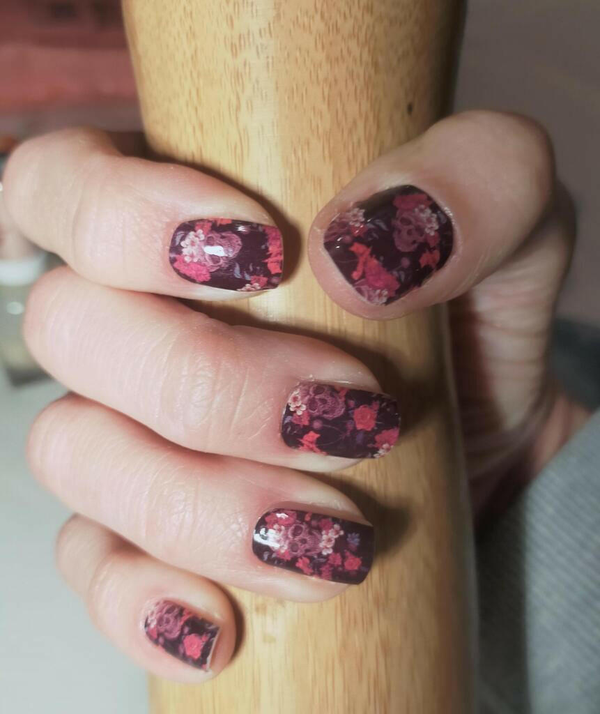 Dark floral skull nail wraps on hand gripping wooden handle
