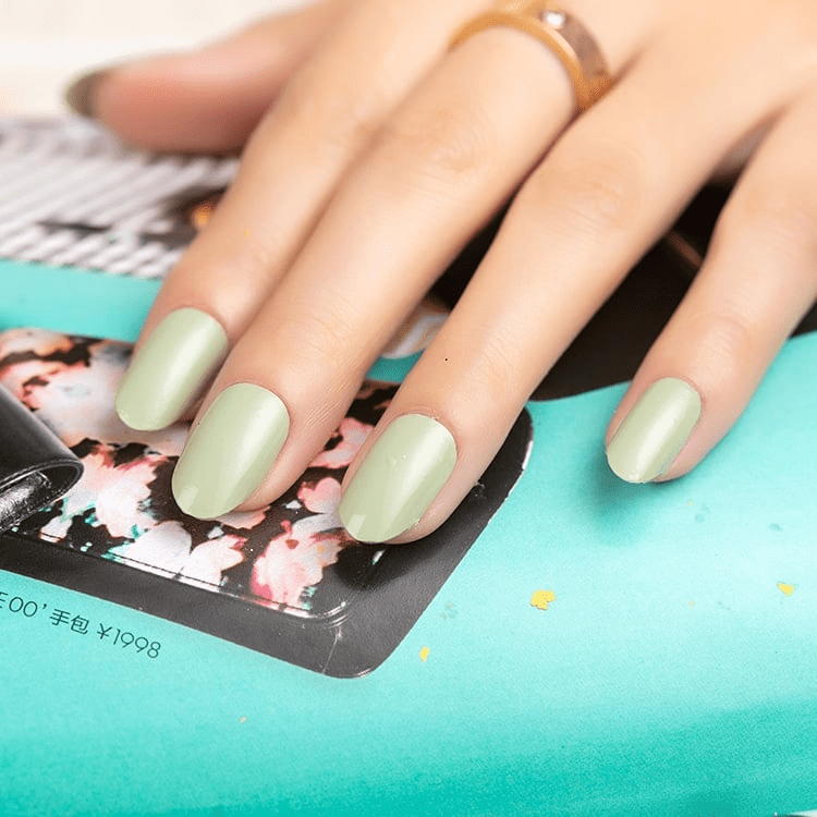 Sage green matte nail wraps on hand resting on colourful magazine for nail art