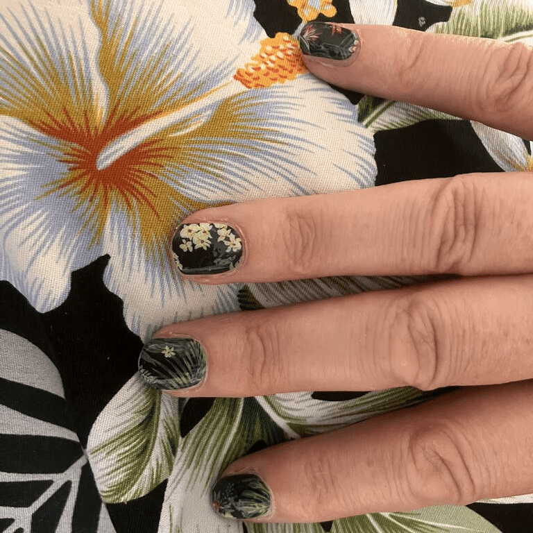 Hand wearing tropical botanical nail wraps featuring green palm fronds and exotic flowers