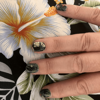 Hand wearing tropical botanical nail wraps featuring green palm fronds and exotic flowers