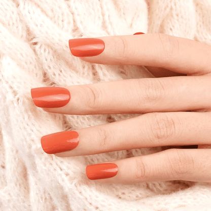 Hand wearing terracotta orange nail wraps against cream knit fabric background