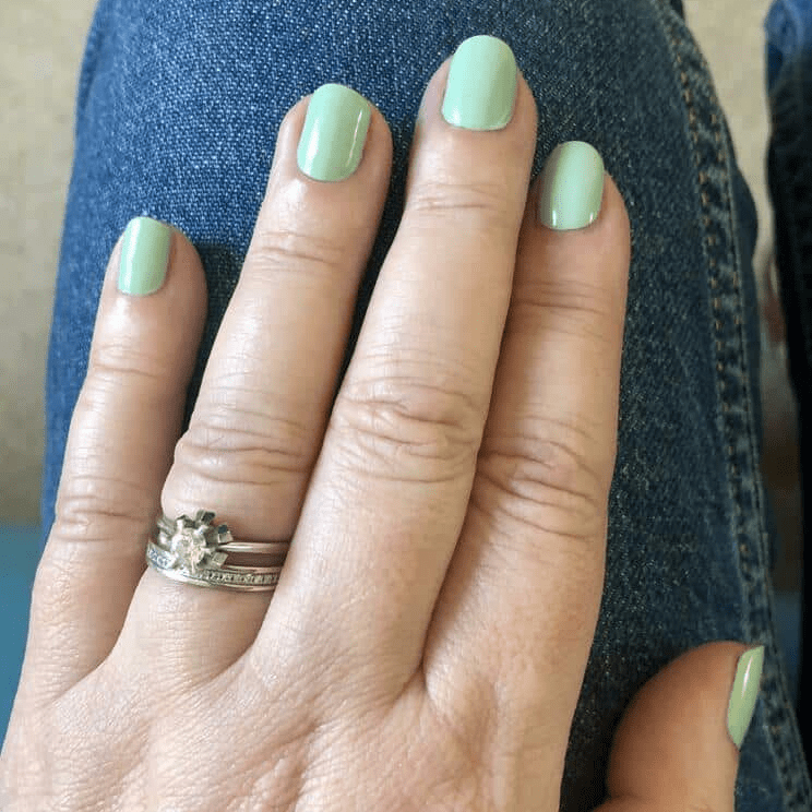 Sage green glossy nail wraps on hand showing muted pastel manicure