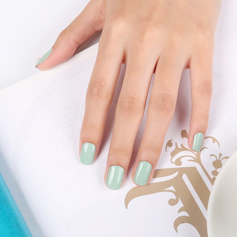 Hand wearing sage green nail wraps showing finished natural green manicure