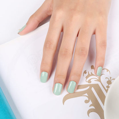 Hand wearing sage green nail wraps showing finished natural green manicure