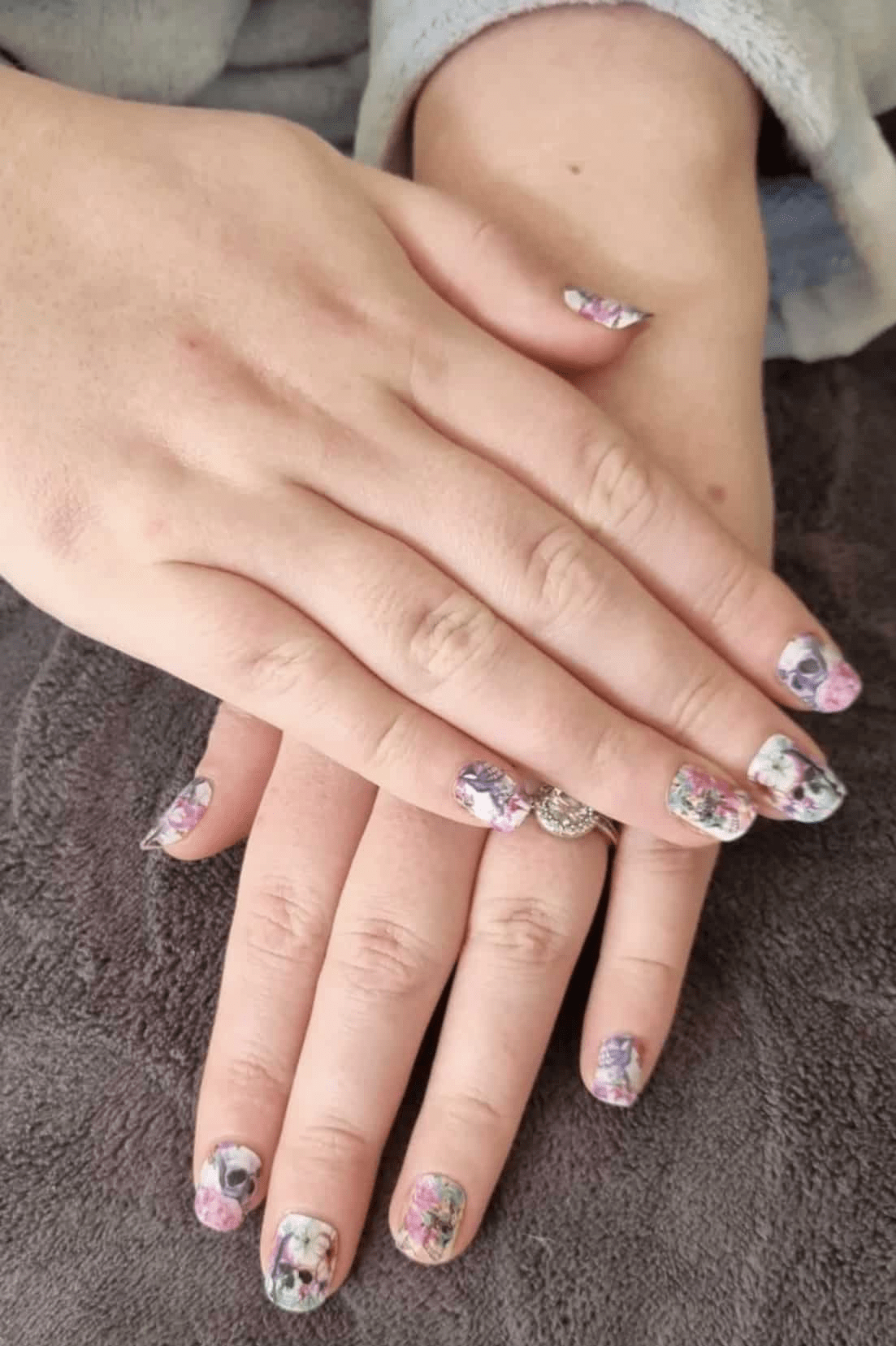 Hands displaying gothic floral nail wraps with pink roses and skull pattern nail art