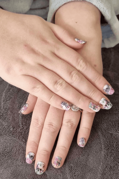 Hands displaying gothic floral nail wraps with pink roses and skull pattern nail art