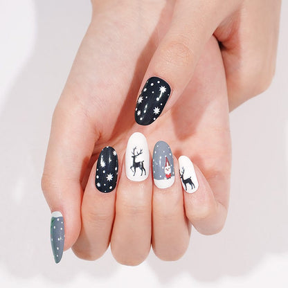 Hand wearing Christmas nail art wraps with navy snowflakes and reindeer designs