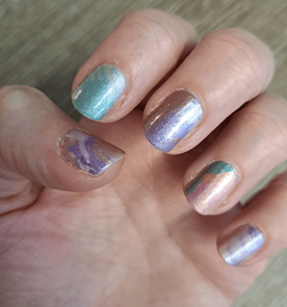 Hand wearing shimmery metallic nail wraps in teal, purple and pink chrome finishes